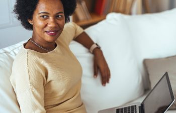 Woman sitting on a couch, using a laptop and looking to the side.