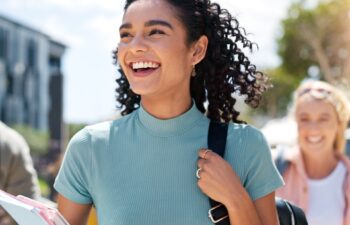 Walking, happy and girl with friends at university for learning, bonding and talking with fun. People, school and group of gen z students commuting outdoor ready for education at college campus.